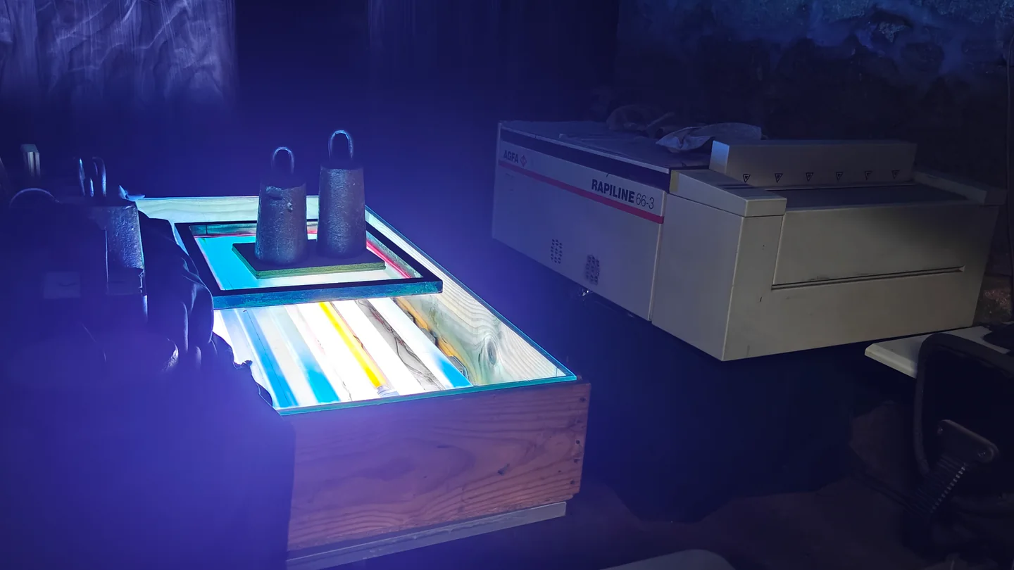 Mesa de exposição iluminada com uma tela pressionada por pesos e, ao lado, uma processadora de película AGFA Rapiline